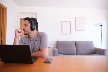 Young man wearing headphones distracted watching series, videos, instead his online classes. Studying online and e-learning concept.