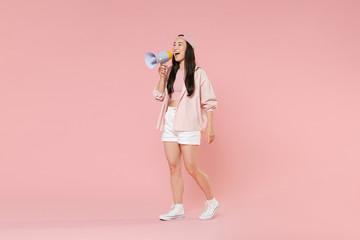Full length portrait of cheerful young asian girl in casual clothes, cap isolated on pastel pink background studio. People lifestyle concept. Mock up copy space. Scream in megaphone, looking aside.