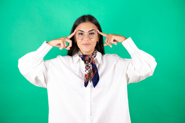 Young beautiful business woman over isolated green background smiling and thinking with her fingers on her head that she has an idea.