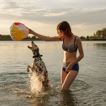 Young attractive girl plays ball with dog in blue lake water