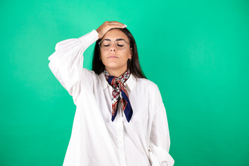 Young beautiful business woman over isolated green background putting one hand on her head smiling...