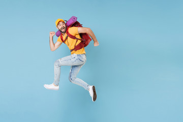 Fototapeta na wymiar Full length portrait Amazed young traveler man in t-shirt cap with backpack isolated on blue background. Tourist traveling on weekend getaway. Tourism discovering hiking concept. Jumping like running.