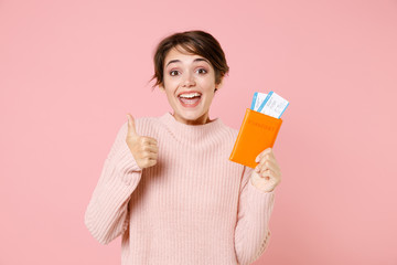 Excited young woman in casual sweater isolated on pastel pink background. Passenger traveling abroad to travel on weekends getaway. Air flight journey concept. Hold passport tickets, showing thumb up.