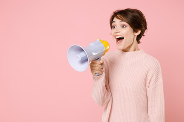 Excited young brunette woman girl wearing knitted casual sweater posing isolated on pastel pink background studio portrait. People emotions lifestyle concept. Screaming in megaphone, looking aside.