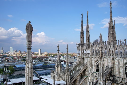 Statue on spire of Milan Cathedral on blue sky background, Milan, Italy. Detail of Gothic roof overlooking Milano city in summer. Nice view of Milan from above