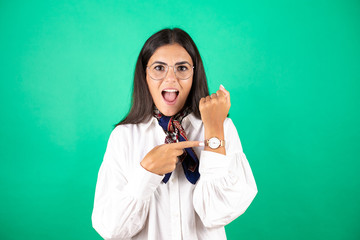 Young beautiful business woman over isolated green background surprised and pointing his watch...
