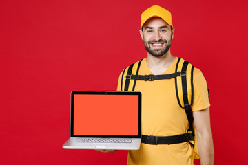 Delivery man in yellow cap t-shirt uniform thermal bag backpack with food hold laptop pc isolated on red background studio Guy male employee work as courier Service coronavirus covid-19 virus concept