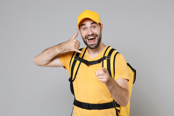 Delivery employee man guy male 20s in yellow cap t-shirt uniform thermal food bag backpack work courier service during quarantine coronavirus covid-19 virus, posing isolated on gray background studio.