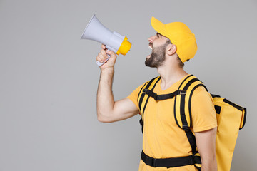 Delivery employee man guy male in yellow cap tshirt uniform thermal food bag backpack work courier service during quarantine coronavirus covid-19 scream in megaphone isolated on gray background studio