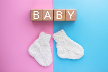 BABY text on wood cubes and pair of cute knitted socks on pink-blue background. Gender of the baby. Boy or girl. Waiting foa a child. Newborn concept.