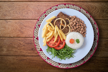 Brazilian food dish. Beans, rice, meat, chips, cabbage, tomatoes, onions. Executive dish. Dish done. Top view. Isolated on wooden background.