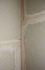 A close-up on drywall corner finishing, plastering, coating with drywall tape or self-adhesive fiberglass mesh over the cracks covered with a layer of joint compound.