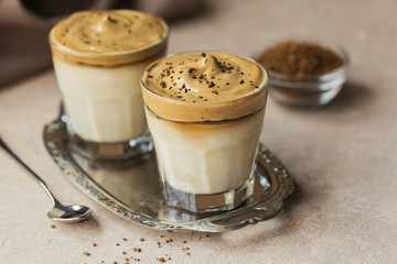 Glass of Iced Dalgona Coffee, trendy fluffy creamy whipped coffee and milk on light beige background.