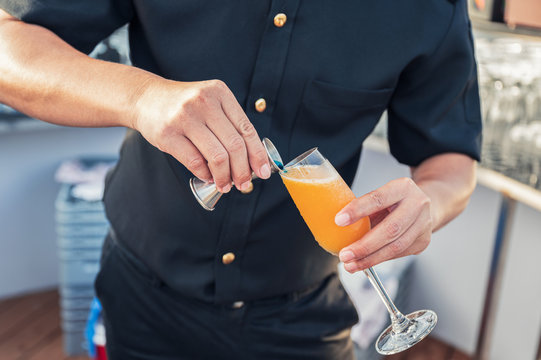 Man bartender mixing cocktail with jugger pouring on wine glass at bar