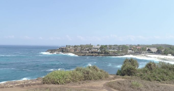 Drone crane shot to reveal white sandy beach and tilt down to waves breaking on rocky coast