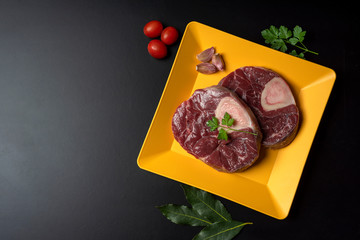 
ossobuco slices on yellow plate with parsley, leek and bay leaf on black background