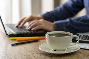 white coffee cup on background of a man working with laptop at home. businessman drinks coffee while working. work at home concept.
