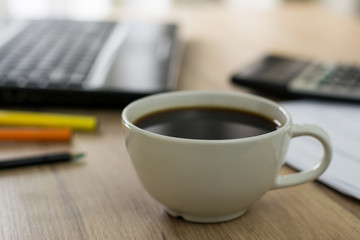 close-up of a white coffee cup with laptop and Calculator on the office desk.
