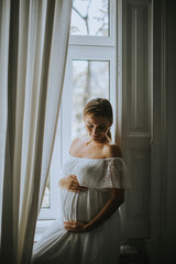 Fototapeta premium Pretty young pregnant woman standing by the windowl in the room