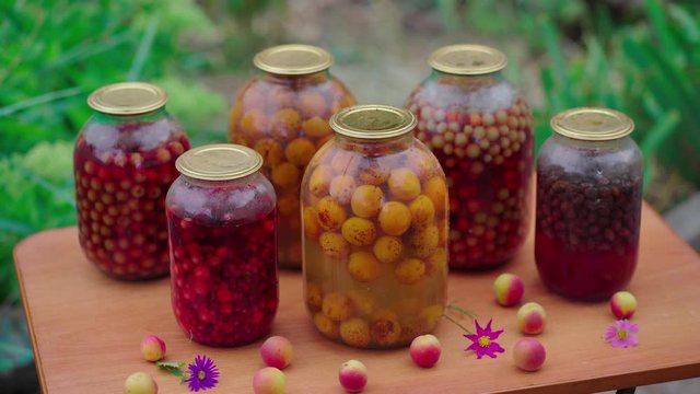 Jars with compote on table. Sealed glass jars with kompot placed on table near flowers and fruits on summer day in garden