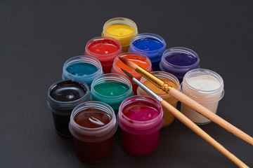 multicolored jars of paint and a brush, on a black background