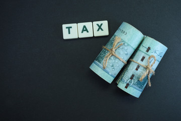 Business tax concept.  Block letters on tax with banknotes on black background