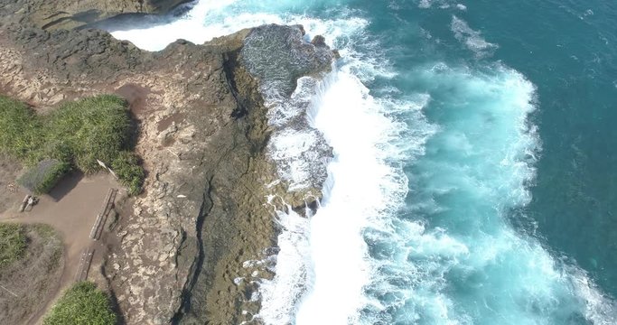 Overhead drone shot looking down onto waves crashing over rock pools on wild coastline