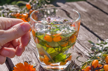 Woman holding a cup with herbal sea buckthorn tea on a wooden background.