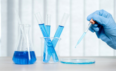Scientists hold the pipette and drop the blue chemical liquid for research and analysis in a laboratory