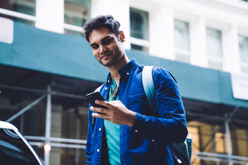 Cool ethnic young man surfing smartphone on street