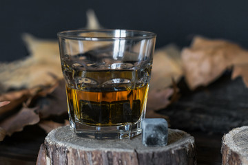 Photo of a glass with amber alcohol and whiskey stones at the bottom and next to it on a wooden stand