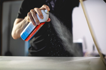 Cropped view of craftsman spraying tack glue on surface of screen printing machine in workshop 