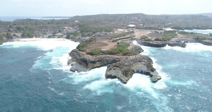 Slow drone orbit around a wild rocky coastline with waves breaking onto rock pools