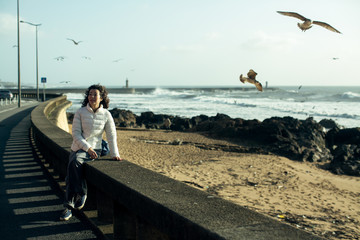 Young multi-cultural woman sitting of sea promenade. Seagulls fly over the foaming surf.