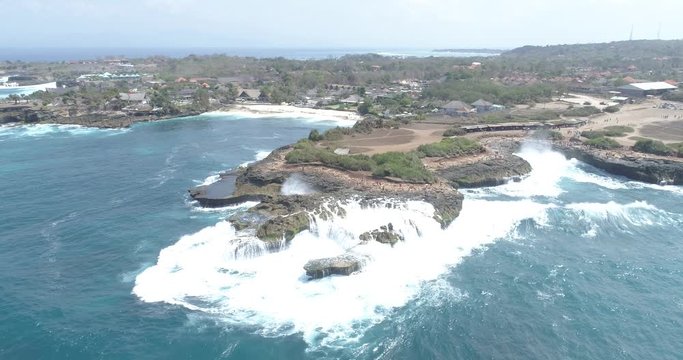 Drone shot tilting down over waves crashing on a wild rocky landscape
