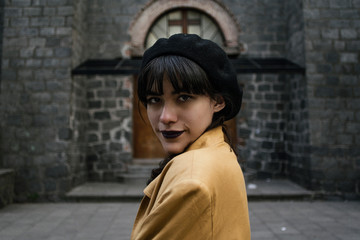 Portrait of a young beautiful latin woman using a black beret outside an old parish