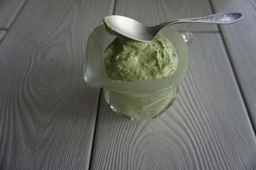 Sauce for fish in a gravy boat, with a spoon on a textured light windowsill.