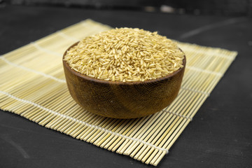 brown rice in a wooden bowl on bamboo mat, asian kitchen background on black