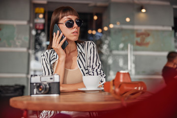 Female in sunglasses is talking on smartphone and is waiting for somebody