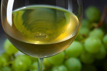 A glass of white wine and white grapes in the background.