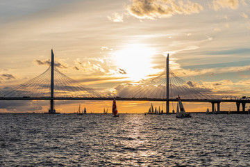 Obraz premium Sailing yacht in the rays of the setting sun on the background of the cable-stayed bridge over the Petrovsky canal