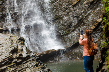 Woman tourist photographs a waterfall .