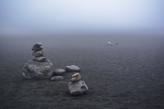 Desolate landscape in a snowy mountain in Nevado del Ruiz with rock stacking in a side, and soil with sand and ashes, neutral colors and mist in the background