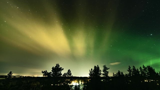 Winter Aurora Borealis green lights over city Umea and northern pine tree forest. Thin cold fog in air makes Northern Lights and stars mixed with city lights unclear and blurry. Sweden,Scandinavia