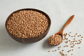 Buckwheat uncooked grains in wooden bowl on gray background close up. Wooden spoon with grits. Healthy, dietary food. Organic, carbohydrate product. Food storage.