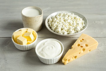 Fototapeta na wymiar Most common dairy products are butter, cheese, milk, sour cream, cottage cheese in white dish on a white wooden background close up. Natural, organic food.