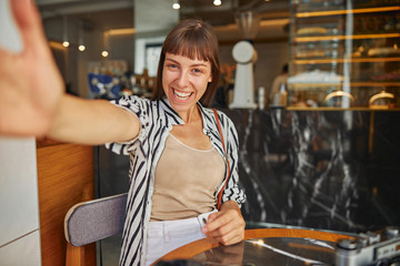 Cheerful young woman photographer with outstretched hand in cafe