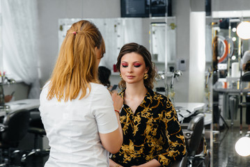 In a beautiful, modern beauty salon, a professional makeup stylist makes makeup for a young girl. Beauty, and fashion