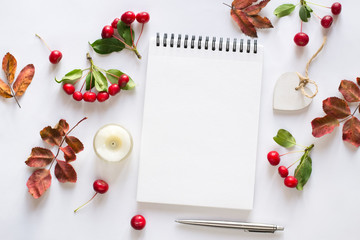 Notepad, red wild apples, leaves, heart, candle on white background. Flat lay. Autumn concept.