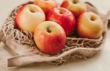 Ripe red apples in a light string bag on a beige background close-up